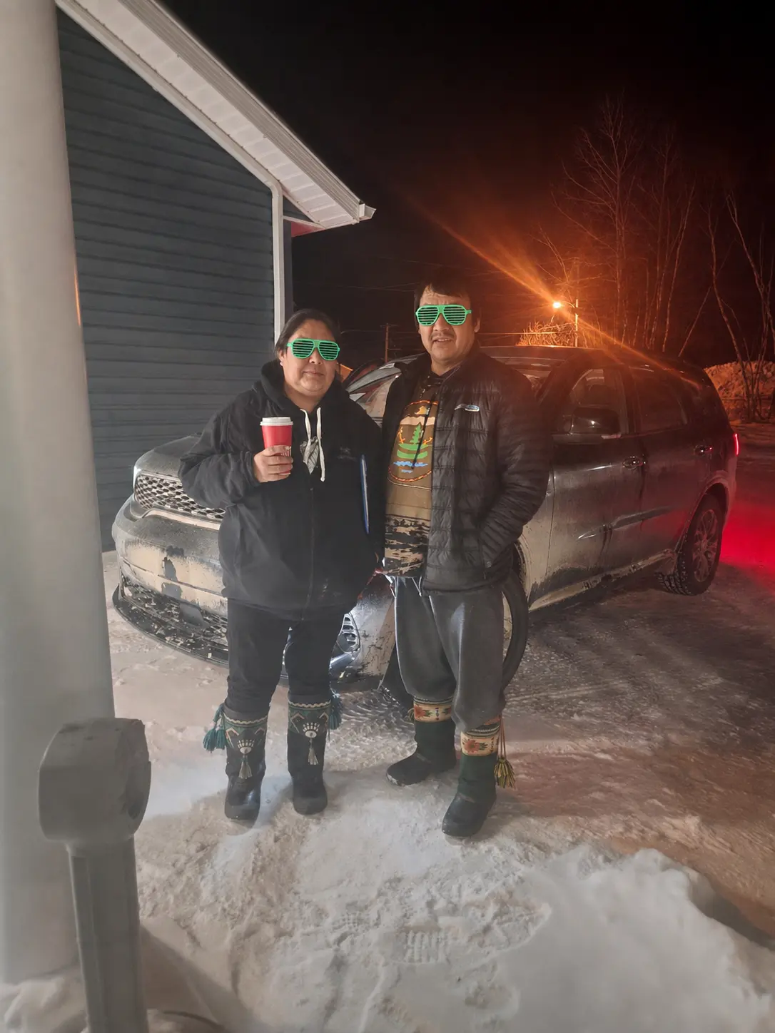 Two customers with a coffee beside their SUV on a winter evening delivery