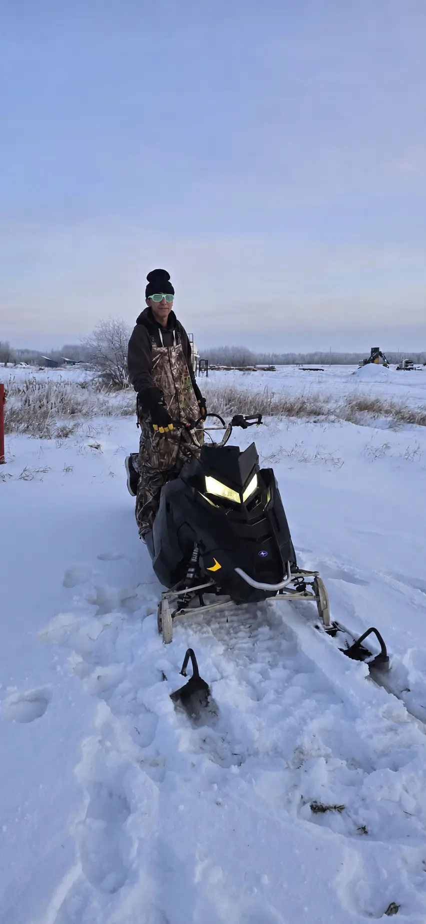 A customer with a black snowmobile at dusk on the snow