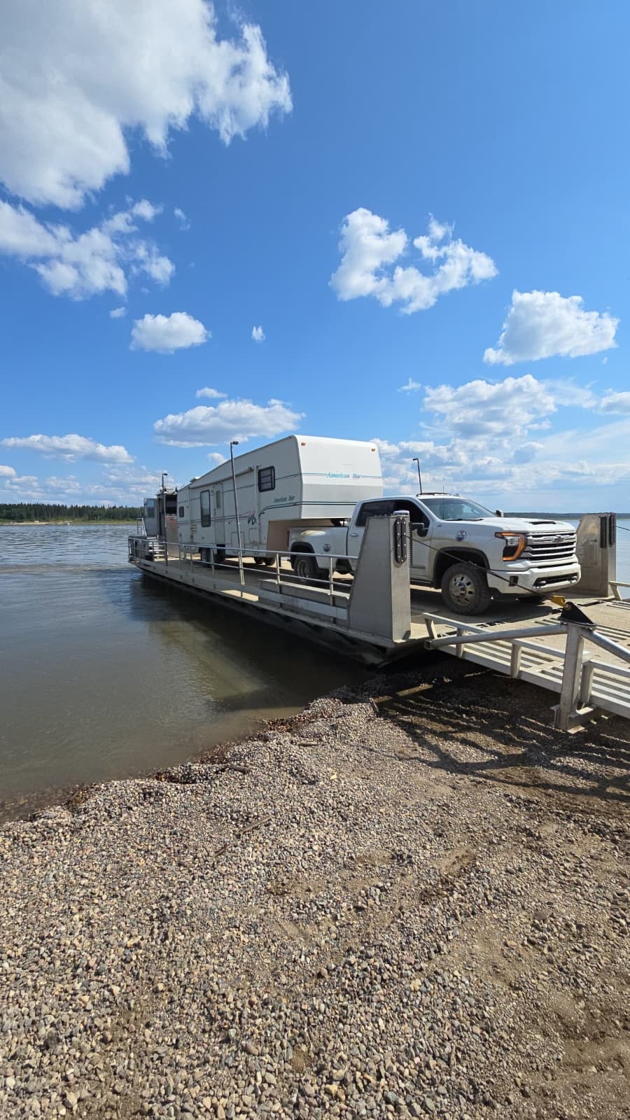 A pickup towing a fifth-wheel trailer crossing a river on a small ferry