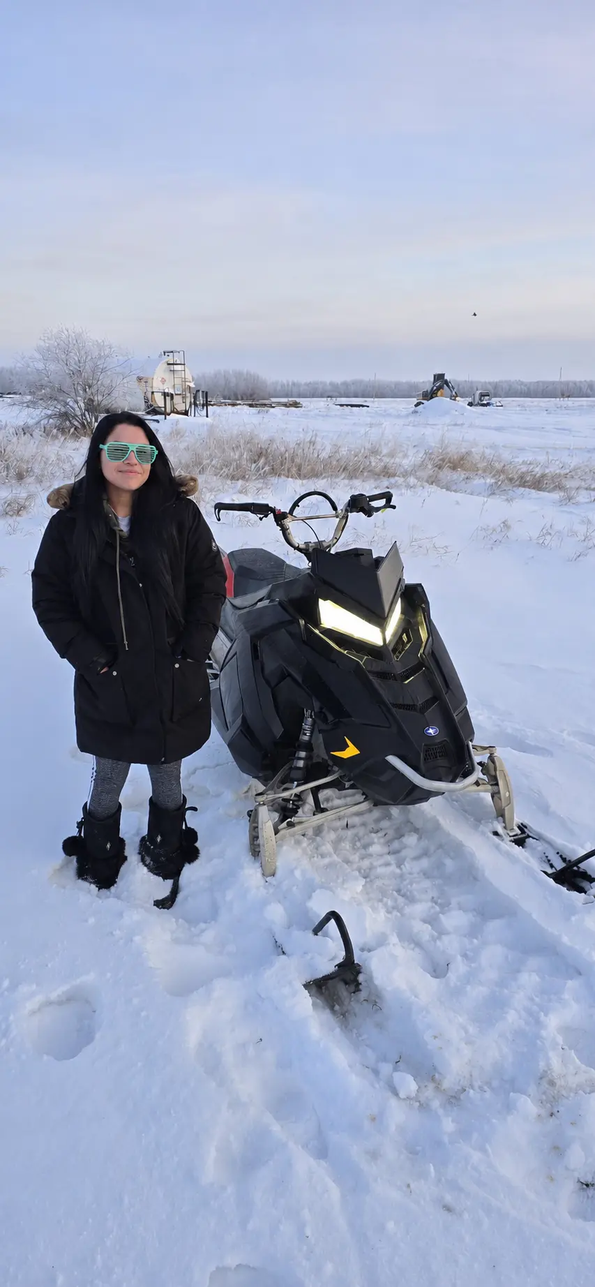 A customer standing with her snowmobile in an open snowy field