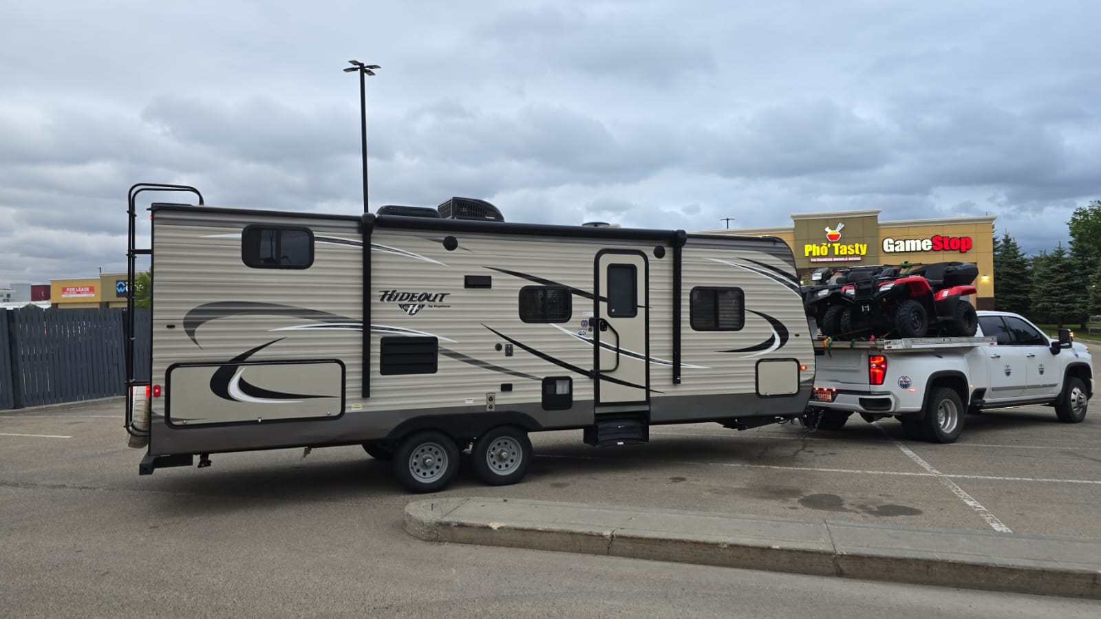 A dually pickup with a travel trailer and two ATVs loaded in the box