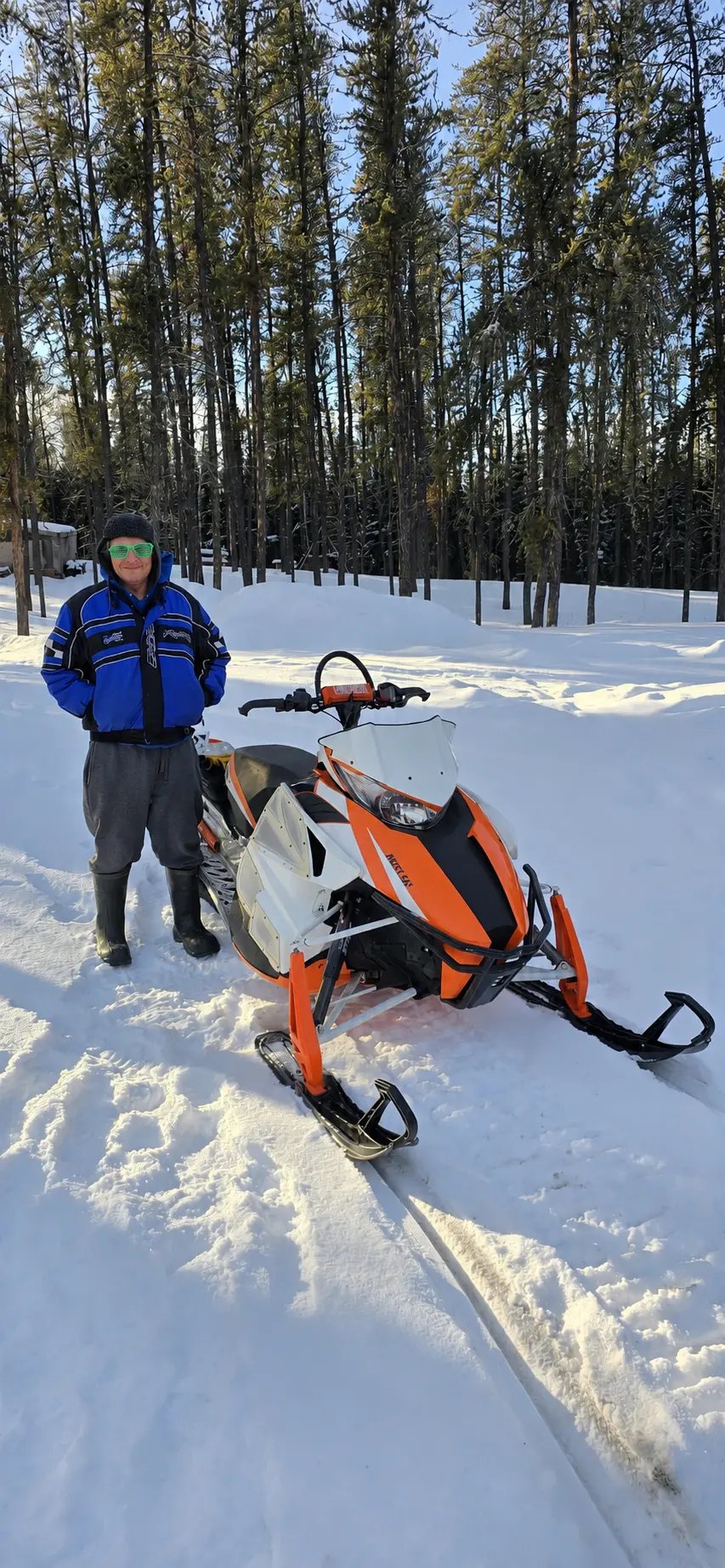 A customer with an orange and white snowmobile in the trees