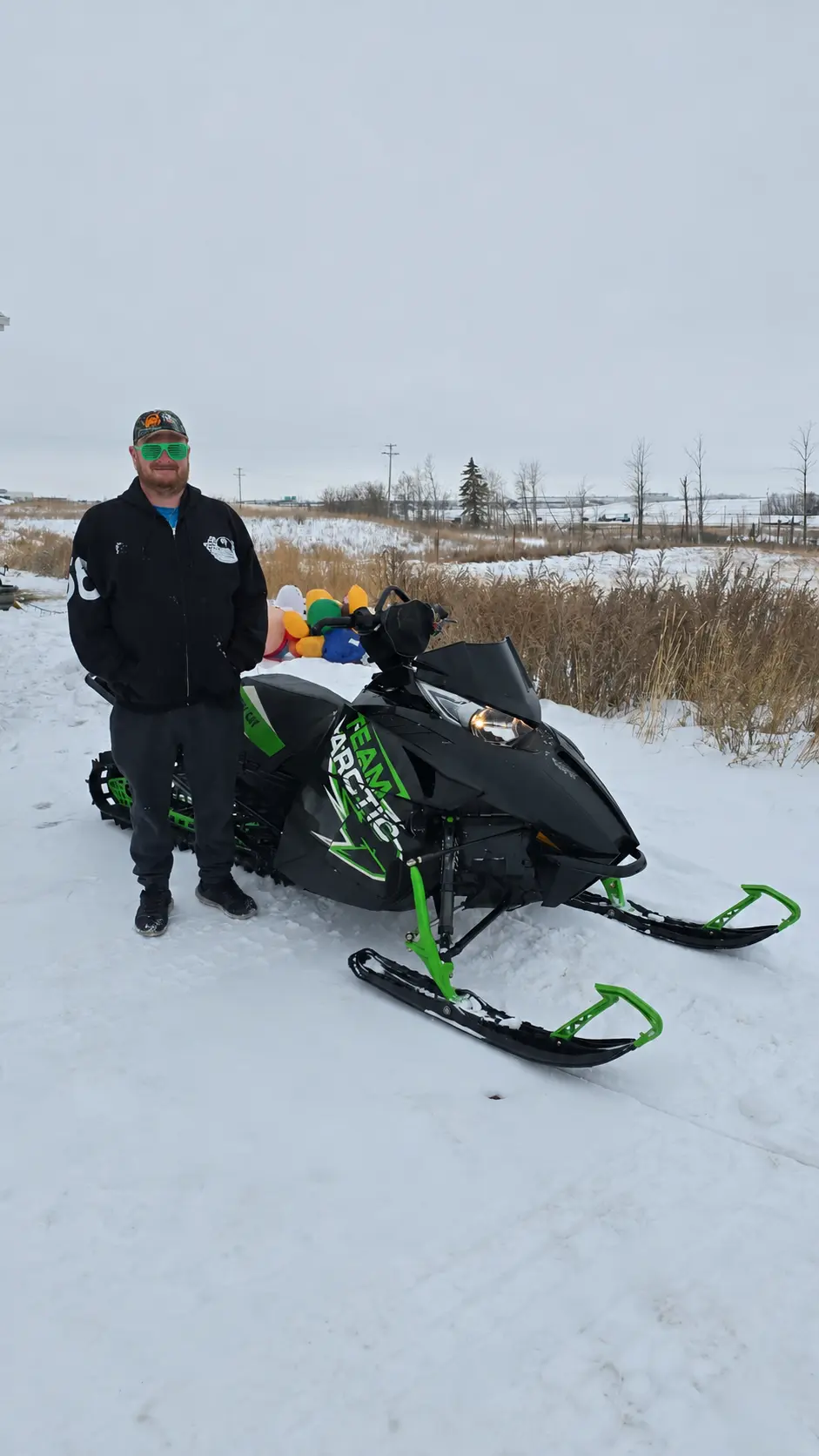 A customer with a black and green snowmobile in a snowy field