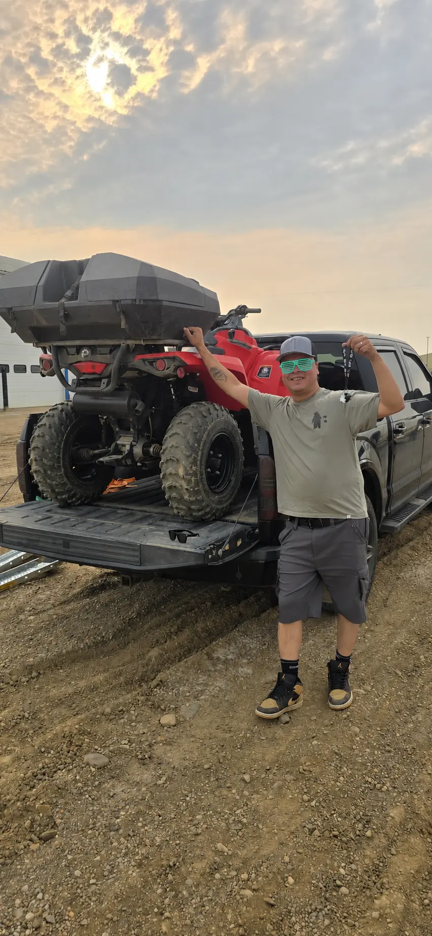 A customer holding up the keys beside a red ATV loaded in a pickup